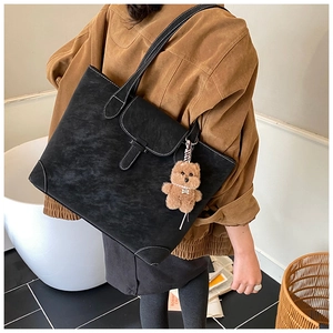 Detail of a large black vintage tote bag with white contrast stitching and a plush bear