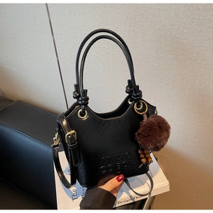 Close-up of black leather bucket bag with top handle, plush charm and brand lettering