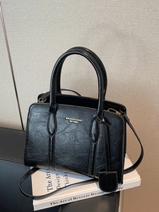 Minimalist black leather crossbody handbag with dual handles and metal logo on a book
