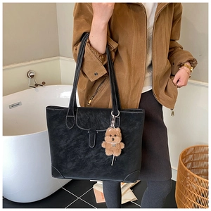 Detail of black matte leather tote bag with white contrast stitching and bear charm