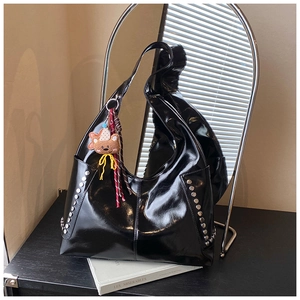 Détails du sac en cuir verni noir avec des rivets argentés et charme d'ours