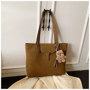 Detail of camel leather tote bag featuring a flap buckle and cute plush bear charm