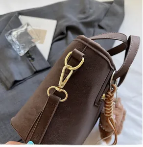 Detail of gold metal hook and lychee pattern leather strap on dark brown crossbody bag