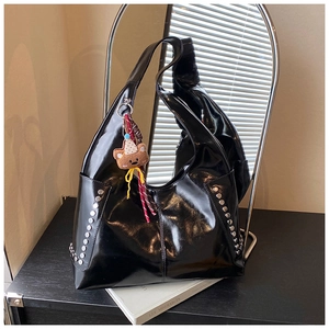 Détail d'un sac à bandoulière noir brillant avec rivets argentés et charm ours mignon