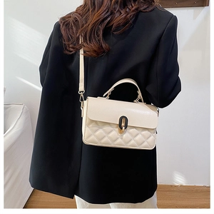 Close-up of off-white quilted handbag featuring a black-gold oval twist lock and handle