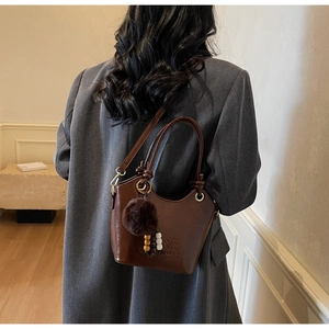 Detail of vintage dark brown bucket bag with plush charm on business blazer model