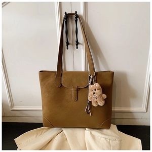 Detail of caramel leather tote bag with decorative strap, snap closure and plush bear charm