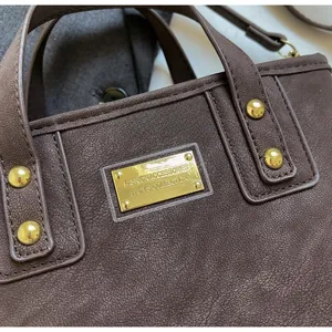 Detail of dark brown leather bucket bag with gold studs and engraved fashion metal plaque
