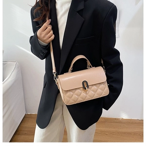 Model wearing a quilted beige leather crossbody bag with an oval black buckle detail