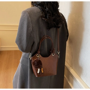 Detail view of brown leather bucket bag with embossed logo and fuzzy pompom charm