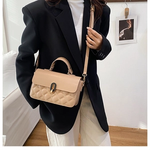 Detail of beige quilted handbag with leather strap and metal twist lock on black blazer