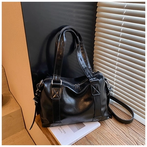 Close-up of a black leather tote bag with cross-stitch handle details and silver zipper