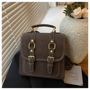 Close-up of vintage dark brown faux leather bag with white stitching and gold buckles