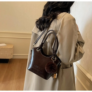 Detail of dark brown leather bucket bag with MKXO COEOR embossing and plush charm