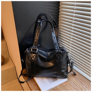 Detail of black glossy leather tote bag showing sturdy handles and metal zipper