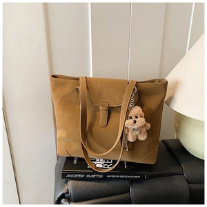Detail of vintage brown tote bag with leather buckle and cute teddy bear charm
