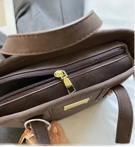 Detail view of dark brown pebbled leather bag featuring a smooth gold zipper and cute bear charm