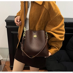 Detail of a dark brown litchi leather bucket bag featuring a gold metal turn-lock closure