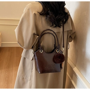 Detail of dark brown glossy bucket bag with MKXQ COEOR embossed logo and fur ball charm