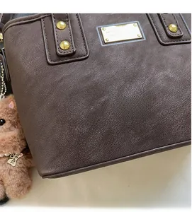Detail of dark brown leather bucket bag with gold rivets and plush animal charm