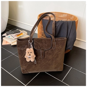 Detail of dark brown vintage leather tote bag with flap buckle and plush puppy pendant