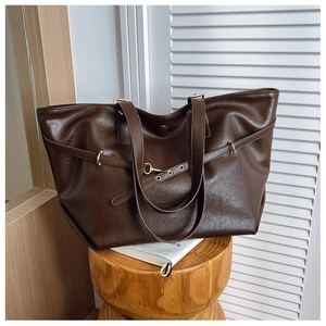 Dettaglio borsa tote in pelle marrone scuro con fibbia dorata su uno sgabello
