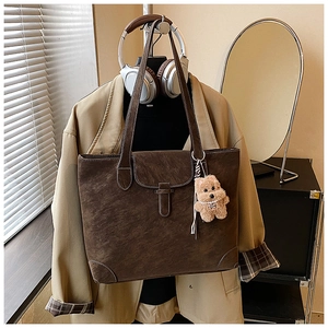 Detail of dark brown suede tote bag with contrast stitching and plush bear charm