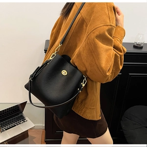 Close-up of black lychee leather texture and golden metal twist lock on bucket bag
