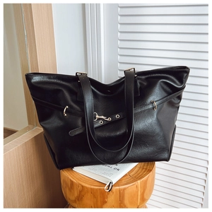 Dettaglio di una borsa tote in pelle nera con fibbie dorate su uno sgabello di legno