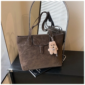 Detail view of vintage dark brown tote bag showing worn leather texture and cute bear charm