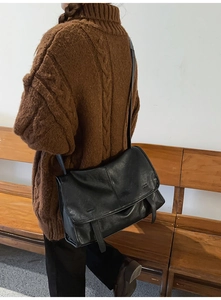 Close-up of a vintage black leather messenger bag worn on shoulder in a retro setting