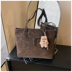 Detail of dark brown faux suede tote bag with white stitching and plush dog charm