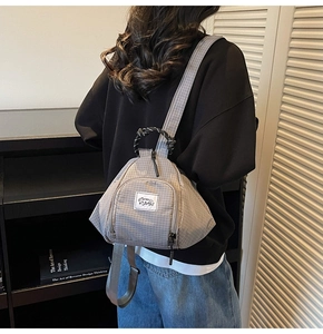 Close-up of grey plaid canvas backpack featuring a triangle shape and front woven logo