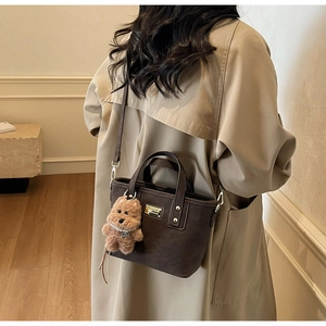 Deep brown tote bag detail with golden metal plate and a cute plush dog charm decoration