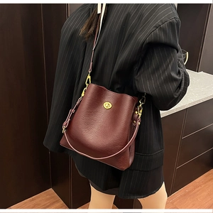 Detail of burgundy lychee leather bucket bag with gold clasp shown on a shoulder
