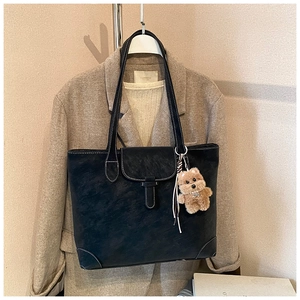 Close-up of black retro tote bag with white stitching and cute brown plush bear charm