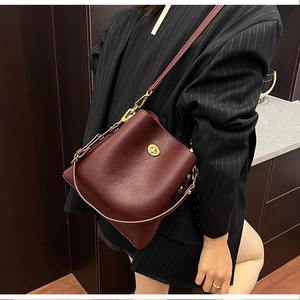 Burgundy bucket bag in pebble leather with gold twist-lock worn with a black pinstripe blazer