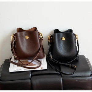Detail view of lychee leather bucket bags in brown and black with gold metal turn-locks
