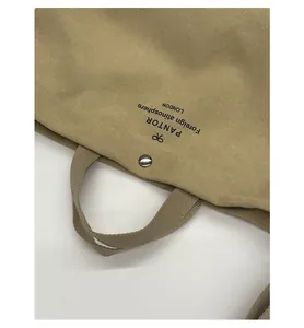 Detail of khaki canvas tote showing thick texture, silver button, and logo print