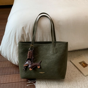 Detail of dark green tote bag with matte texture, gold logo, and cute doll pendant