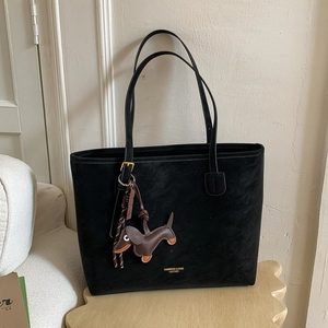 Detail of black matte leather tote bag with a brown dachshund charm on a sofa
