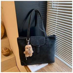 Detail of dark tote bag with contrast white stitching and brown plush bear charm