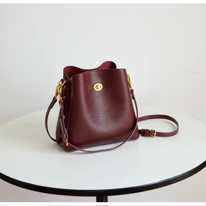 Detail of burgundy pebbled leather bucket bag with gold turn-lock and adjustable strap
