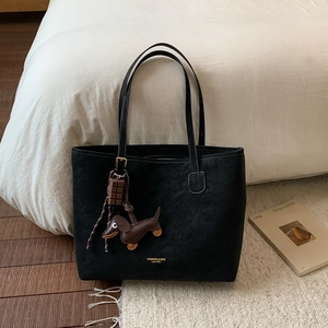 Close-up of black leather tote bag with dachshund charm and gold logo detail