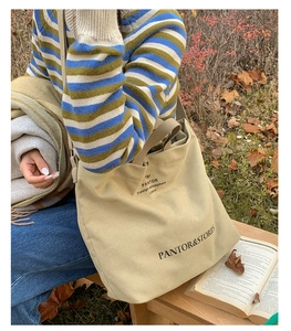 Detail of khaki canvas tote bag with black letter print and ribbon in autumn outdoor setting