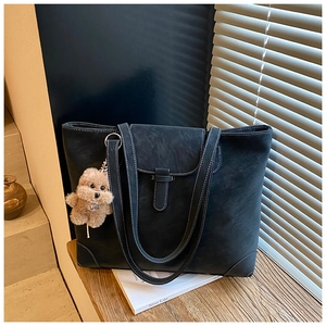 Close-up of black tote bag with white contrast stitching and a plush teddy bear charm