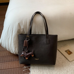 Detail of dark brown leather tote bag with gold lettering and decorative pendants