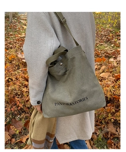 Detail of dark green canvas tote bag with black letter print in autumn outdoor setting