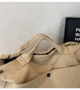 Detail of warm khaki canvas shoulder bag showing cross-stitched handles and metal snap button