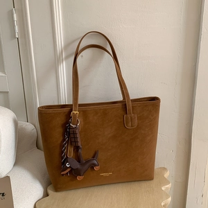 Detail of a brown leather tote bag featuring a sausage dog and chocolate bar charm